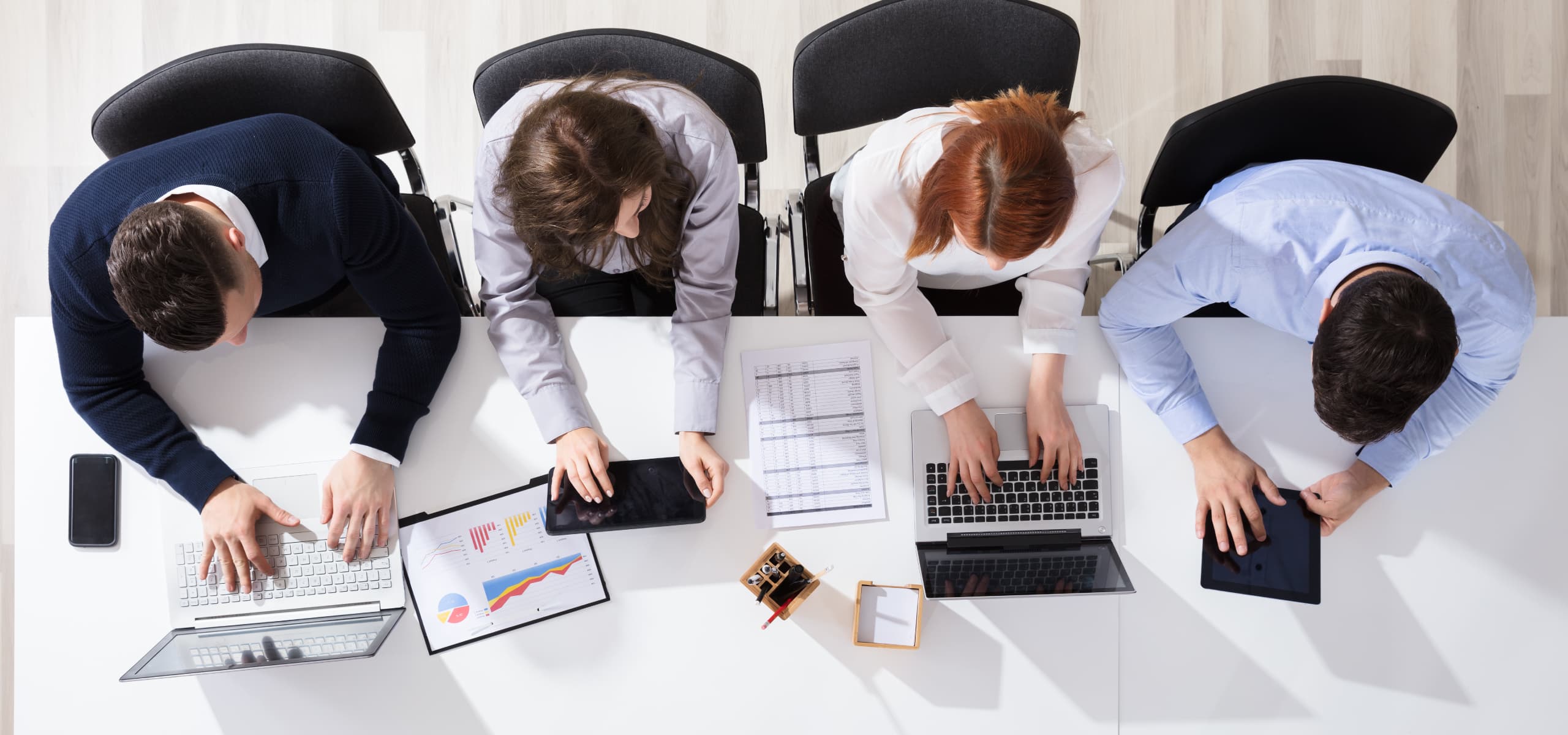 People working on laptops around a desk, viewed from above