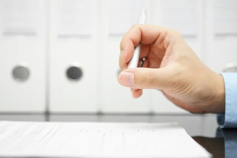 Close up a writer's hand holding a pen over a CV